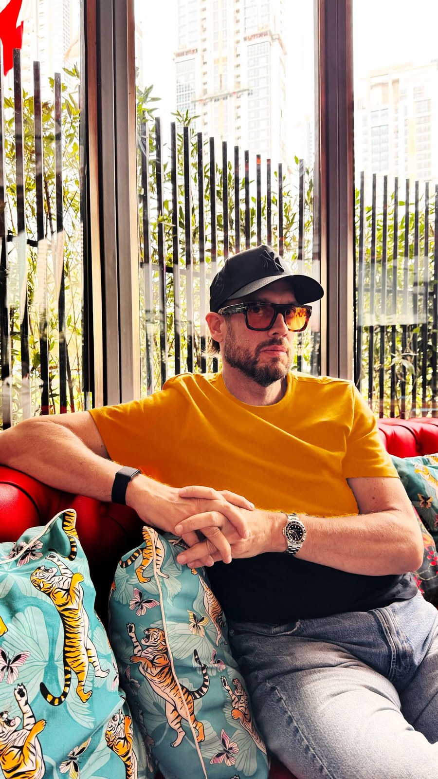 Mano González in a yellow T-shirt and cap, sitting on a red sofa with tiger cushions